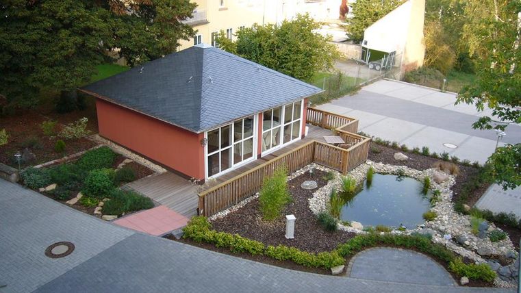 Ein schönes Gartenhaus mit einem modernen Design steht in einem gepflegten Garten. Umgeben von Pflanzen und einem kleinen Teich, bietet es einen ruhigen Rückzugsort.