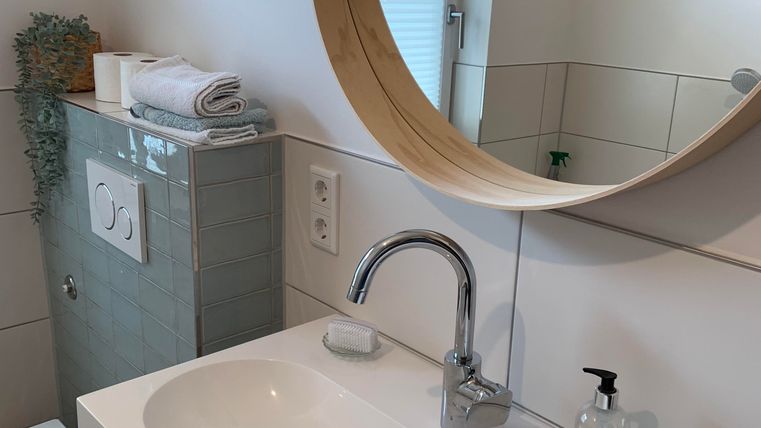 Een modern badkamer met een ronde spiegel en een elegant wastafel. Op de achtergrond zijn handdoeken en een kleine plant te zien.