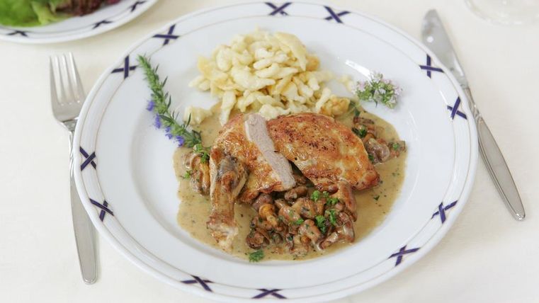 Ein köstliches Gericht mit gebratenem Hähnchen, Pilzen und einer cremigen Sauce. Dazu gibt es frische Spätzle und etwas grüne Kräuter.