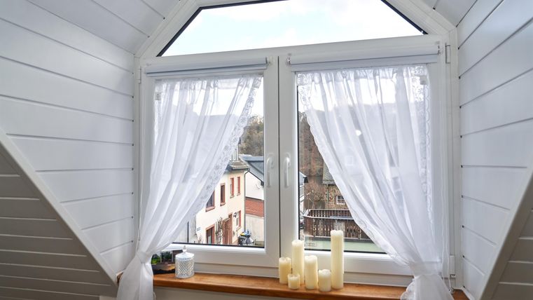 A window with white curtains and a view of a cityscape. There are some candles on the windowsill.