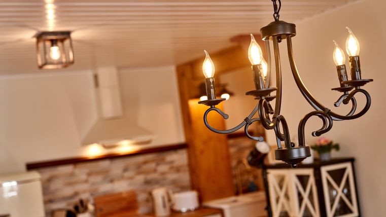 A modern kitchen with an elegant chandelier and warm light. In the background, kitchen cabinets and appliances are visible.