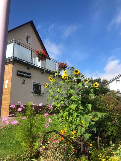 Ein schönes Haus mit Balkon und Blumenkästen. Vor dem Haus blühen Sonnenblumen und andere bunte Blumen im Garten.