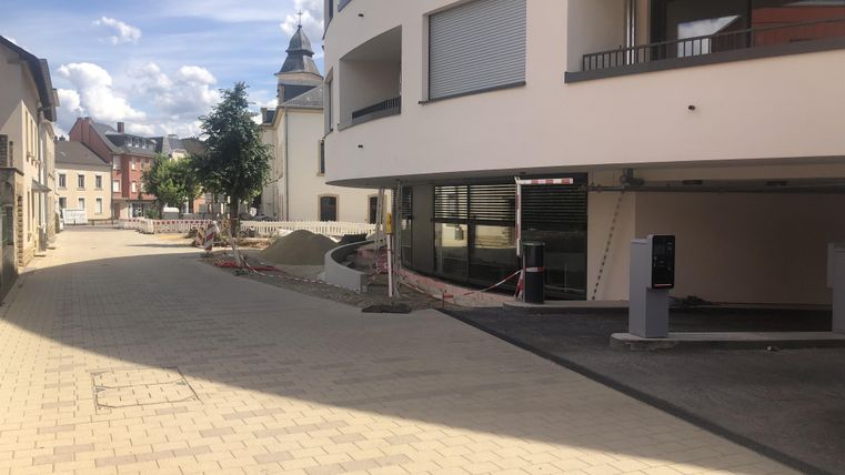 A quiet street with modern buildings and plenty of daylight. On the left side, trees and construction materials are visible.