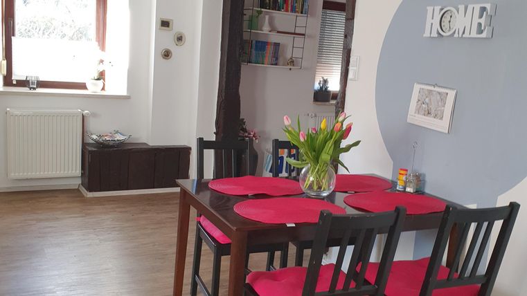 Een gezellige eetruimte met een tafel en stoelen in zwart en rood. Aan de muur hangt het woord "HOME" en er is een heldere sfeer door het raam.