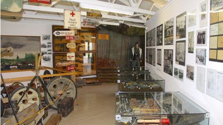 Een museum met historische artefacten, waaronder gereedschappen en foto's aan de muren. In het midden staat een standbeeld, omringd door vitrines met verschillende tentoonstellingsstukken.