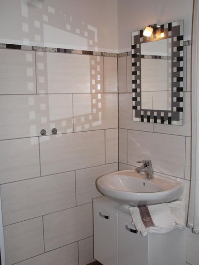 A modern bathroom with a bright wall covering and a sink. The mirror has a graphic design and there is a ceiling light.