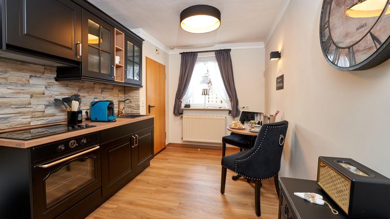 A modern kitchen with dark cabinets and a wooden floor. The dining area is cozily furnished and features a table and a chair.