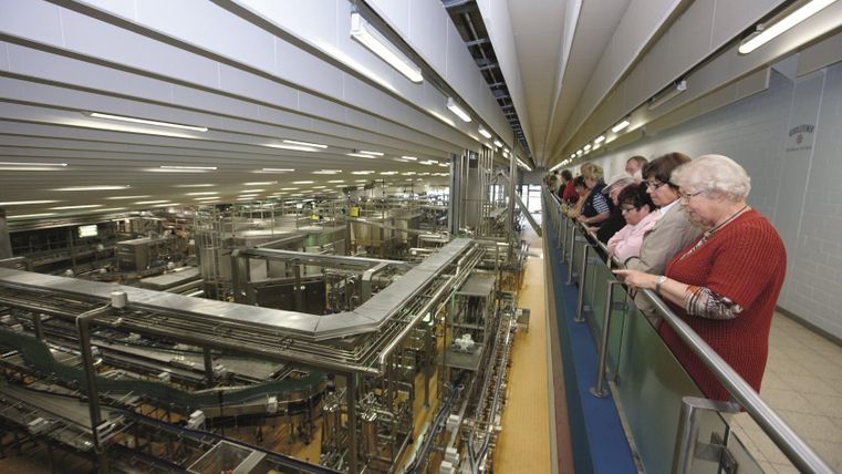 Visitors stand on a gallery and look at the bottling plant in the Gerolsteiner Spring Visitor Center. Industrial environment with machines.