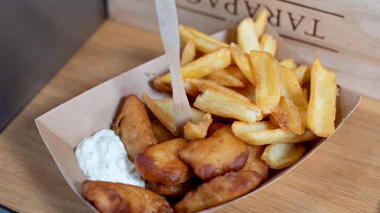 Een eettype met knapperige frietjes en gefrituurde kipstukjes. Daarbij is er een portie saus in een klein bekertje.