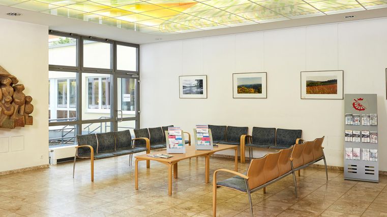 Ein moderner Wartebereich mit bequemen Sitzen und Kunstwerken an den Wänden. Ein Informationsstand und ein Automat sind ebenfalls sichtbar.