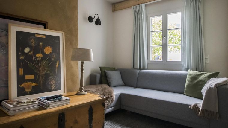 Ein gemütliches Wohnzimmer mit einem grauen Sofa und einer dekorativen Lampe. Neben dem Sofa steht ein Holztisch mit einem Kunstwerk und einigen Büchern.