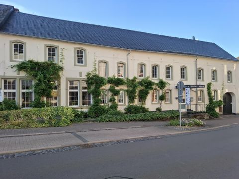 Ein charmantes Gebäude mit weißen Wänden und grünen Pflanzen. Die Fenster sind groß und einladend, und die Umgebung ist gepflegt.