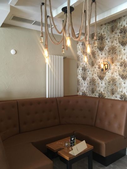 Eine gemütliche Sitzecke mit braunen Polstern und einem eleganten Kronleuchter. Die Wand ist mit floralen Mustern verziert und schafft eine einladende Atmosphäre.