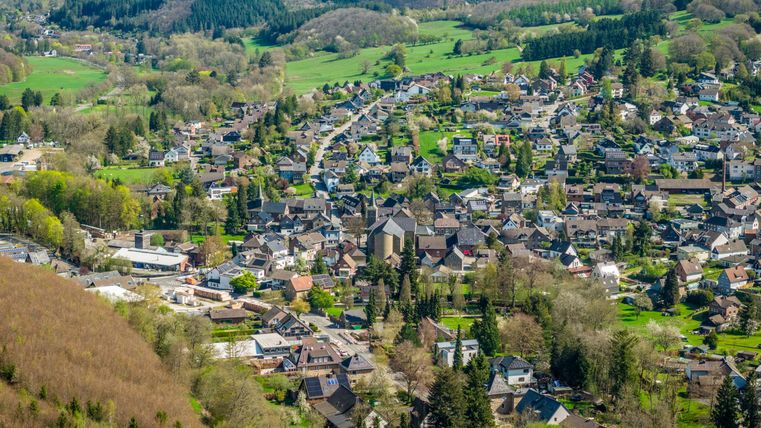 Eine malerische Ansicht eines kleinen Dorfes mit vielen Häusern und grünen Wäldern in der Umgebung. Die sanften Hügel und die klare Landschaft vermitteln ein ruhiges und idyllisches Gefühl.
