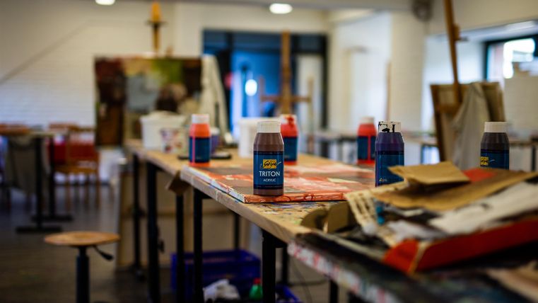 Eine kreative Künstlerumgebung mit Tisch, Farben und Malutensilien. Der Raum ist gut beleuchtet und lädt zum Malen ein.