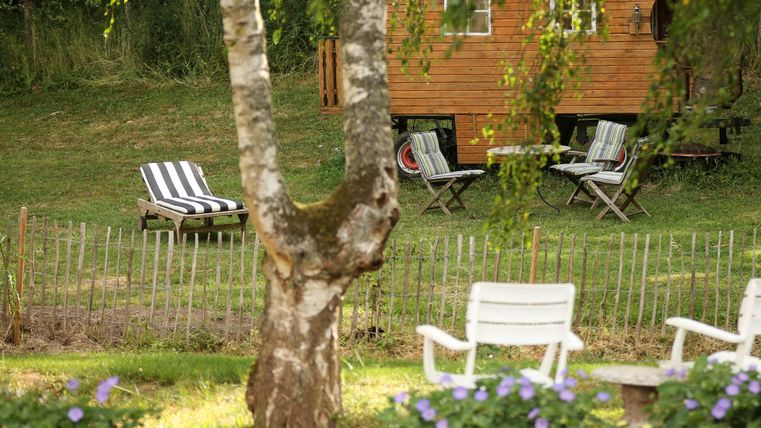 A cozy outdoor area with a wooden house in the background and several loungers. Flower beds and a small fence give the place an inviting atmosphere.