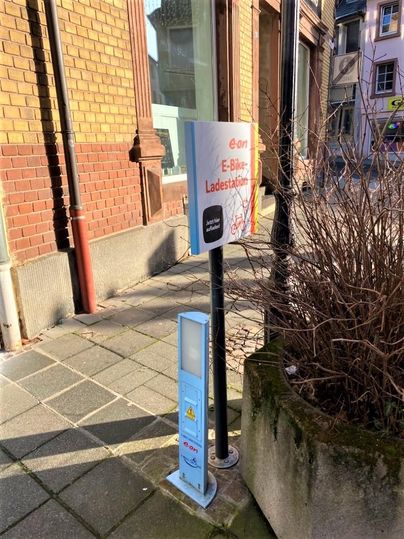 An E-bike charging station is located on a sidewalk. The area is well-maintained, with a sign indicating the charging option.