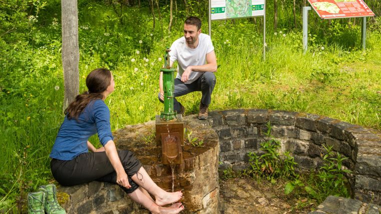 Two people at the Demerather Drees on the Vulcano Trail, one cooling her feet in the water.