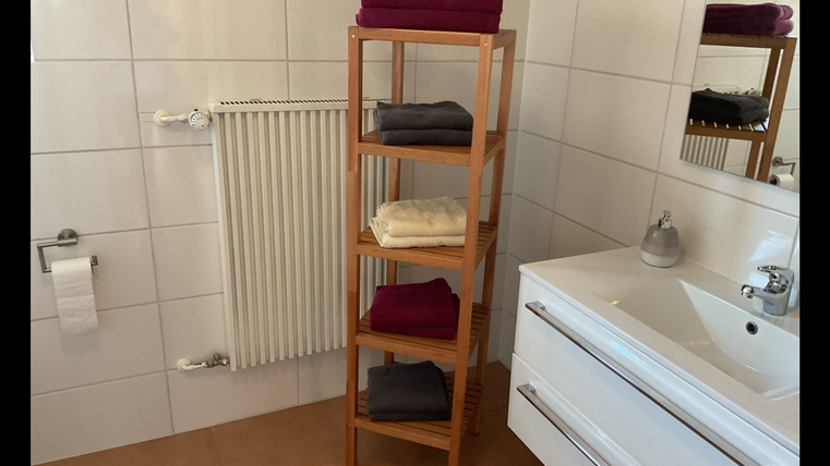 A modern bathroom with a wooden shelf displaying neatly folded towels in various colors. In the background, a sink and a mirror can be seen.