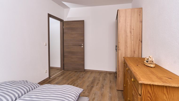 Ein einfaches Schlafzimmer mit einem Bett und gestreiften Bettdecken. An einer Wand befindet sich eine Holzkommode und ein Schrank.