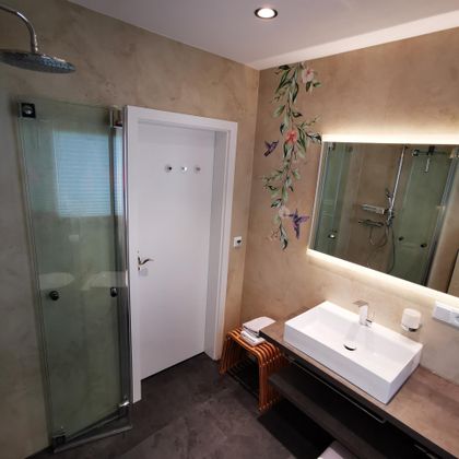 Een moderne badkamer met een glazen douche en een elegant washok. Aan de muur zijn decoratieve plantenmotieven te zien.