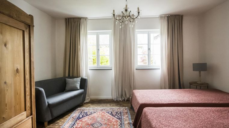 Ein helles Schlafzimmer mit zwei Einzelbetten und einem gemütlichen Sofa. Die großen Fenster lassen viel Tageslicht herein.