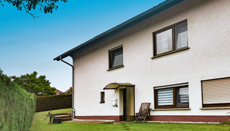 Ein modernes Haus mit einem gepflegten Garten. Die Fassade ist hell und einladend, umgeben von Bäumen und Rasenflächen.