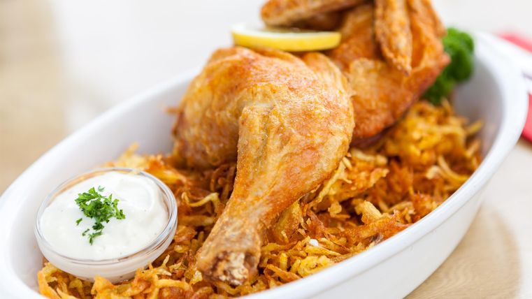 A delicious dish with crispy chicken, served on a bed of fried potatoes. Accompanied by a portion of sauce and fresh lemon.