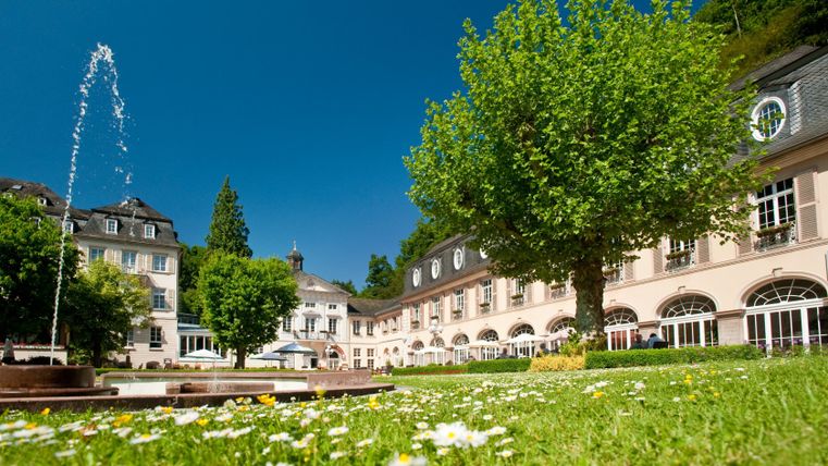 Historisches Gebäude mit Springbrunnen und blühender Wiese in Bad Bertrich.