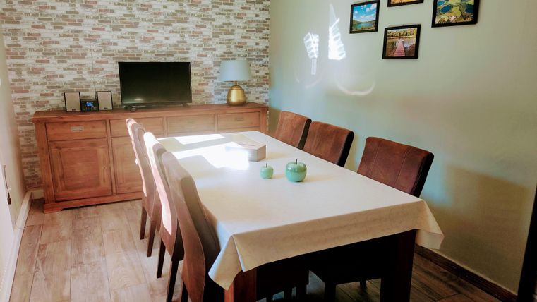 A cozy dining area with a large table and eight chairs. On the wall are pictures and a television.