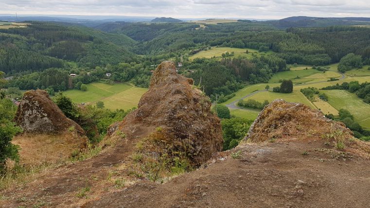 Een uitzicht op groene heuvels en valleien onder een bewolkte hemel. Rotsen rijzen op in de voorgrond en bieden een blik op het natuurlandschap.