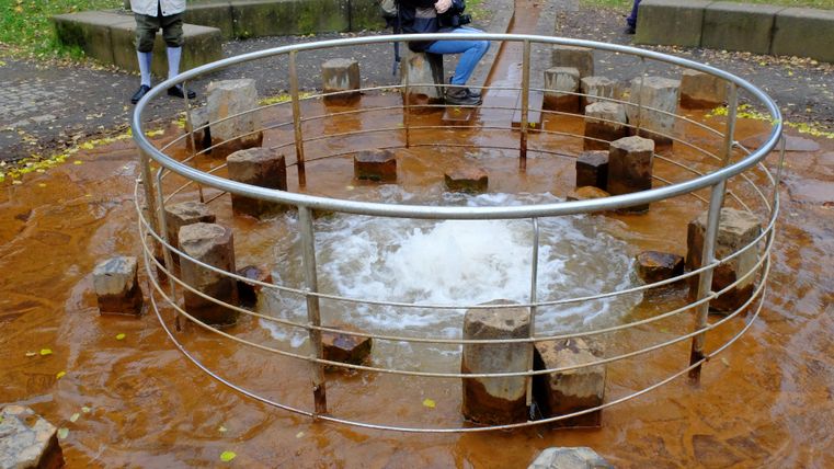 A round water area surrounded by wooden logs. In the center, the water is bubbling.