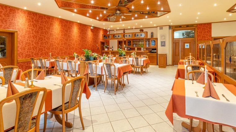 Een uitnodigend restaurant met elegante tafels en warme verlichting. De muren zijn in een chique rood ontworpen, wat een gezellige sfeer creëert.