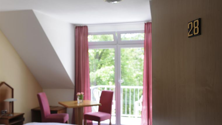 Ein gemütliches Zimmer mit einem Tisch und zwei Stühlen. Große Fenster sorgen für viel Tageslicht und einen Blick ins Grüne.