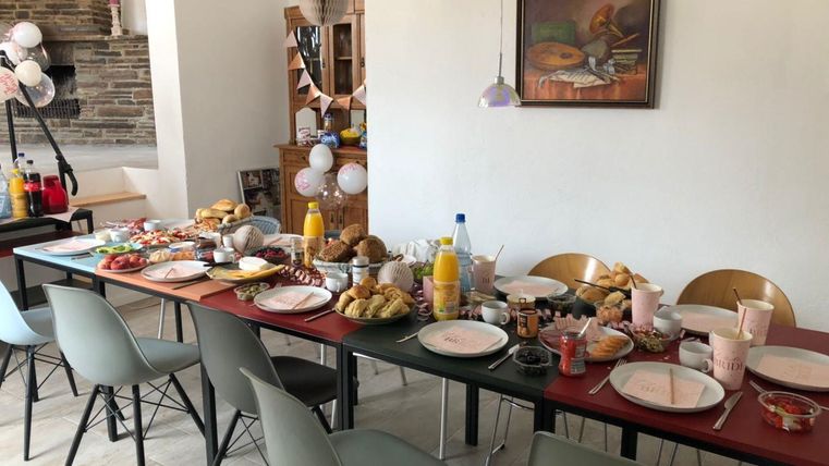 Ein festlich gedeckter Tisch mit verschiedenen Speisen und Getränken. Rund um den Tisch stehen gemütliche Stühle und es gibt dekorative Elemente.