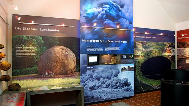 Ein Teil eines Museums mit Ausstellungsgriffen zu Vulkanausbrüchen. An den Wänden sind Informationsgrafiken und Bilder von Lava und Naturphänomenen zu sehen.