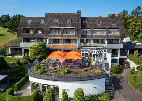Een modern hotel met de naam „Hotel Panorama“ en een uitnodigend terras. Het terras is versierd met oranje parasols en groene planten.