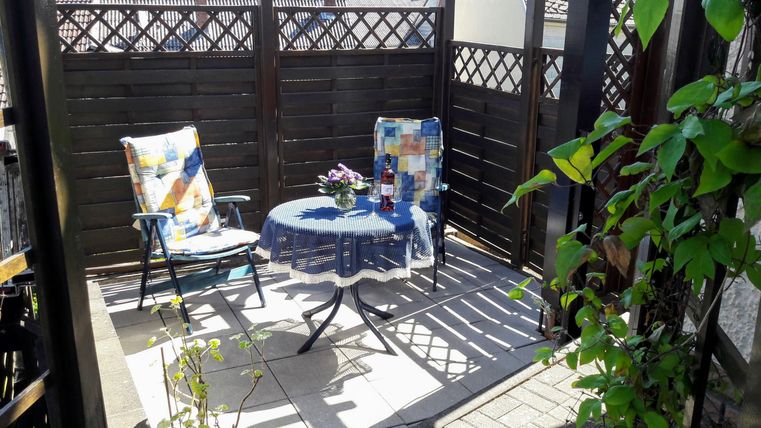 Een gezellige terrazza met twee stoelen en een kleine tafel. Omringd door groene planten en een houten privacy-scherm.