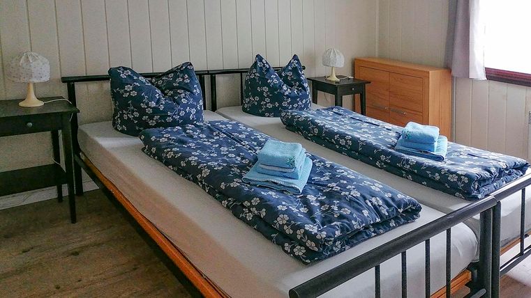 Een gezellige kamer met twee bedden, elk met blauwe dekens en kussens. Naast de bedden liggen frisse handdoeken en er zijn kleine nachtkastjes met lampen.