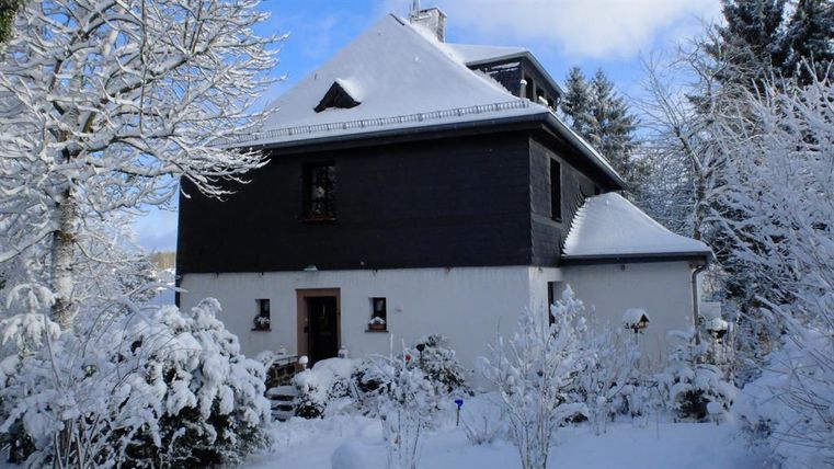 Een prachtig huis, omringd door met sneeuw bedekte bomen en struiken. De lucht is helder en blauw.
