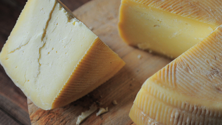 Ein großer Käseblock wurde angeschnitten und liegt auf einem Holztablett.