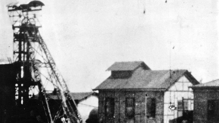Een historisch industriegebouw met een mijnbouwtoren. De omgeving lijkt verlaten en vertoont tekenen van slijtage.