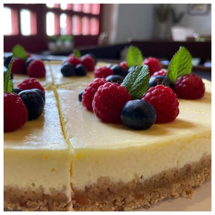 Ein köstlicher Käsekuchen mit einer glatten, cremigen Oberfläche. Er ist mit frischen Himbeeren, Blaubeeren und Minzblättern dekoriert.