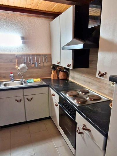 A modern kitchen with bright cabinets and a dark workspace. The room features a rustic wooden ceiling and is well-lit.