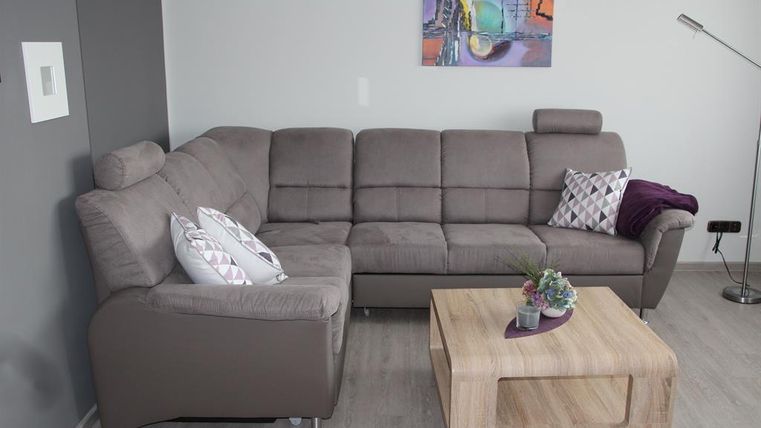 A modern living room with a gray couch and a wooden table. A colorful painting hangs on the wall, and there are decorative cushions on the couch.