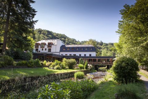 Ein elegantes Hotel inmitten einer grünen Landschaft. Umgeben von Bäumen und einem ruhigen Gewässer bietet es eine idyllische Atmosphäre.