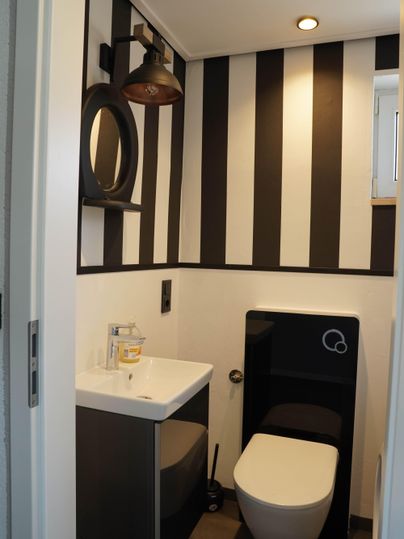 Ein modernes Badezimmer mit schwarz-weiß gestreiften Wänden. Es enthält ein Waschbecken, einen Spiegel und eine elegante Toilette.