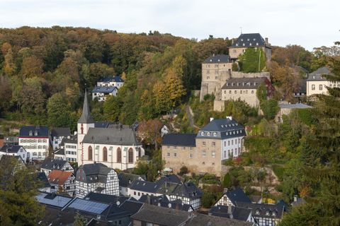 Eine malerische Landschaft mit einem historischen Schloss und einer kleinen Stadt. Bunte Bäume umgeben die Gebäude im Herbst.