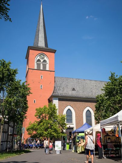 A magnificent church with a tall, pointed tower stands in the background. In front of the church, a market is taking place with stalls.