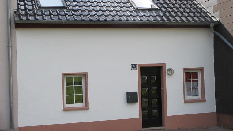 Ein einfaches, zweigeschossiges Haus mit einem grauen Dach. Es hat weiße Wände und grüne Fenster mit einem schlichten Eingangsbereich.